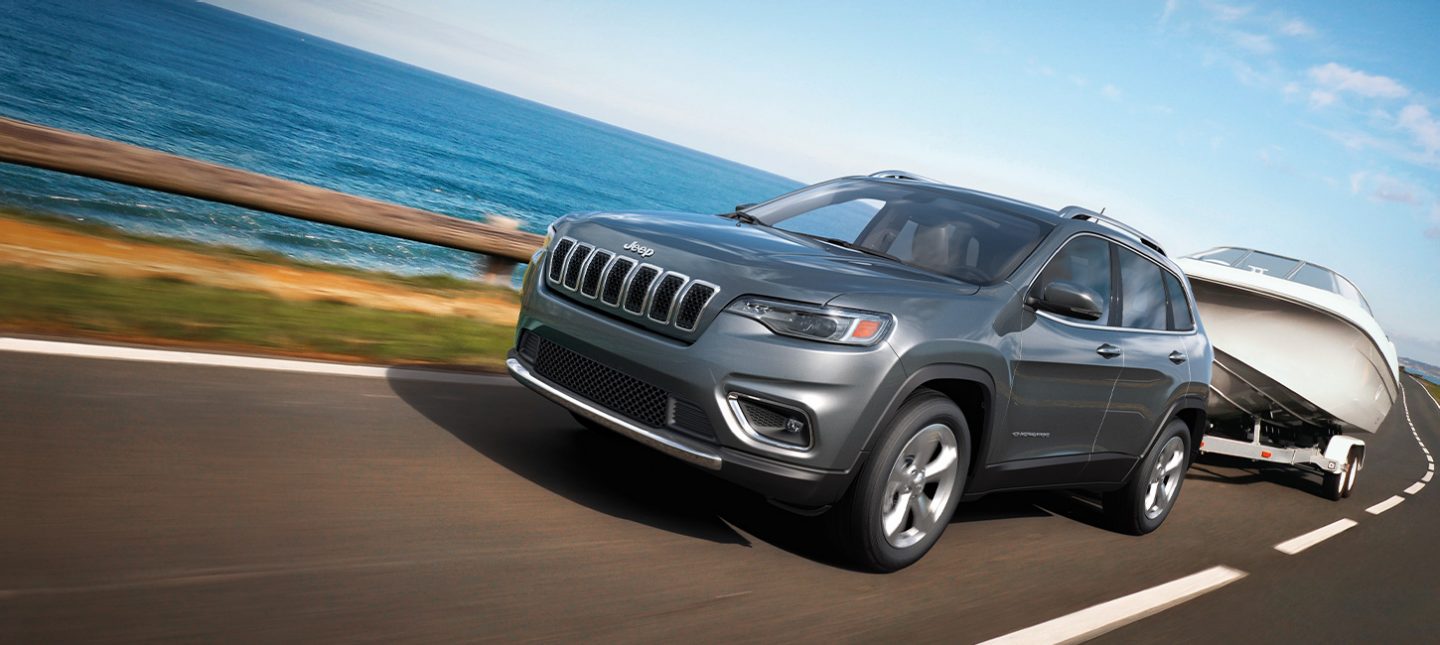 The 2020 Jeep Cherokee Limited towing a boat on a two-lane highway.