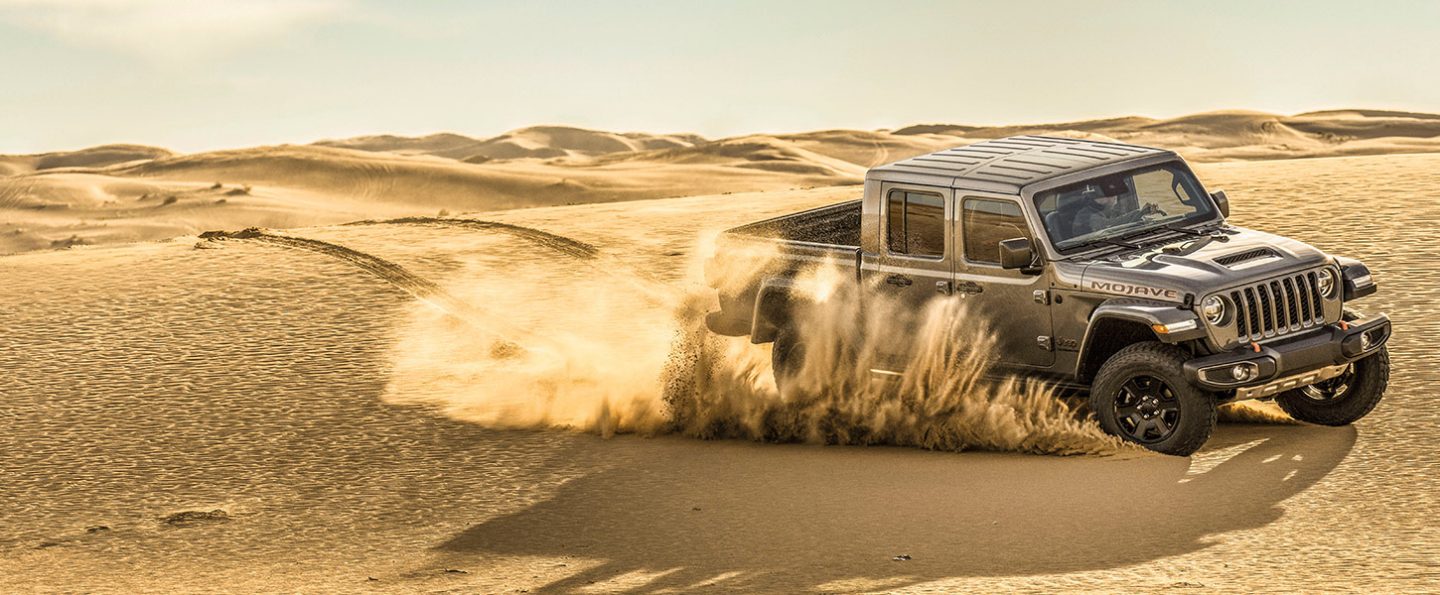 The 2020 Jeep Gladiator Mojave churning up sand as it is driven through the desert.