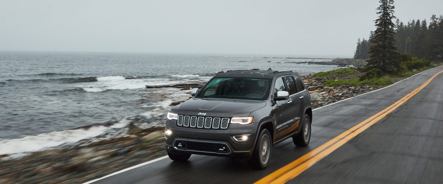 The 2020 Jeep Grand Cherokee being driven along a seaside highway.