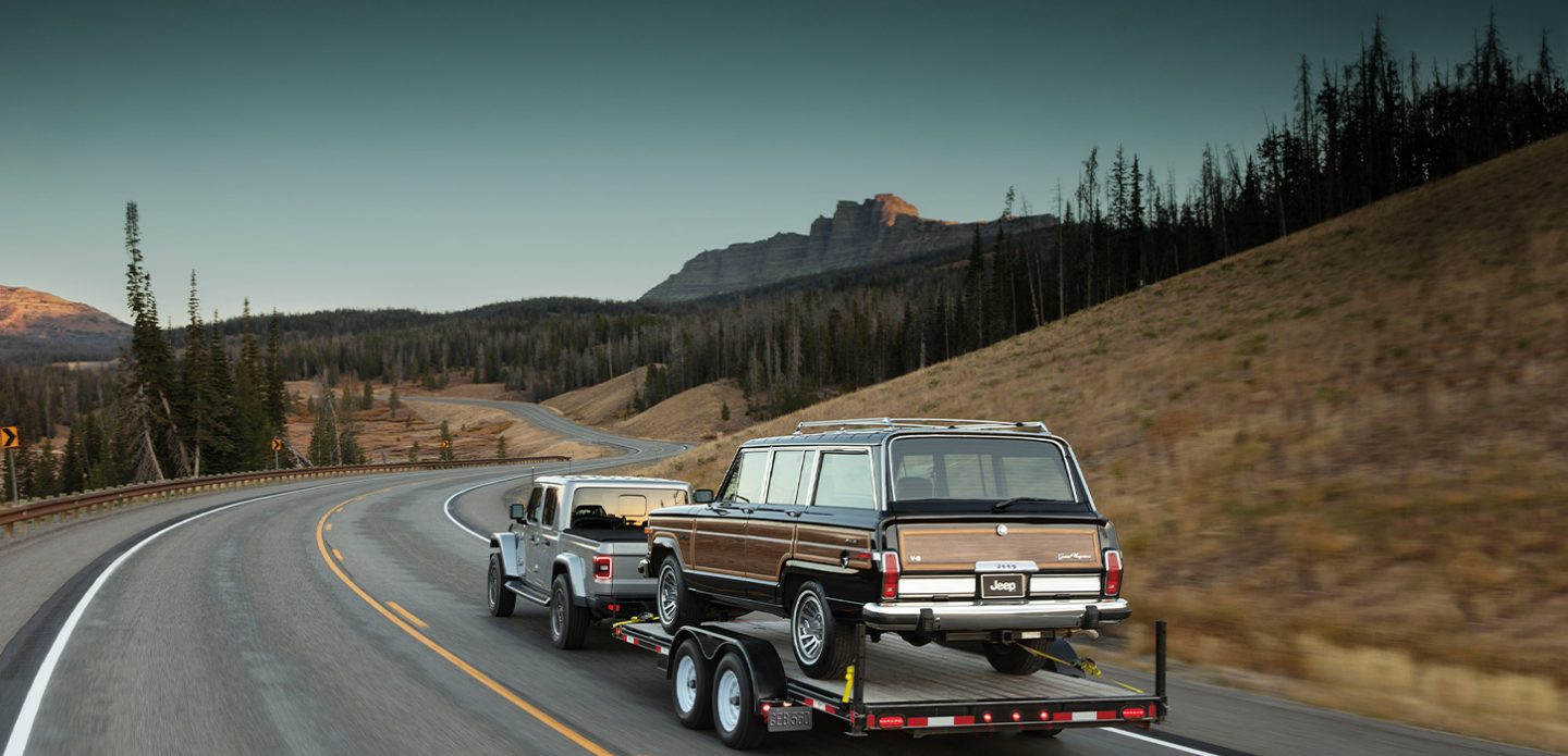 The 2021 Jeep Gladiator Overland towing a trailer with an older Jeep Grand Wagoneer on it.
