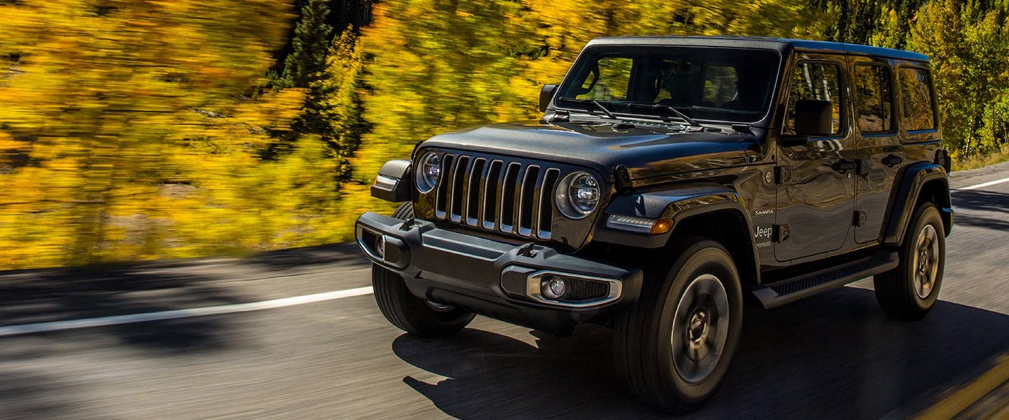 The 2021 Jeep Wrangler Sahara being driven on a highway in the woods.