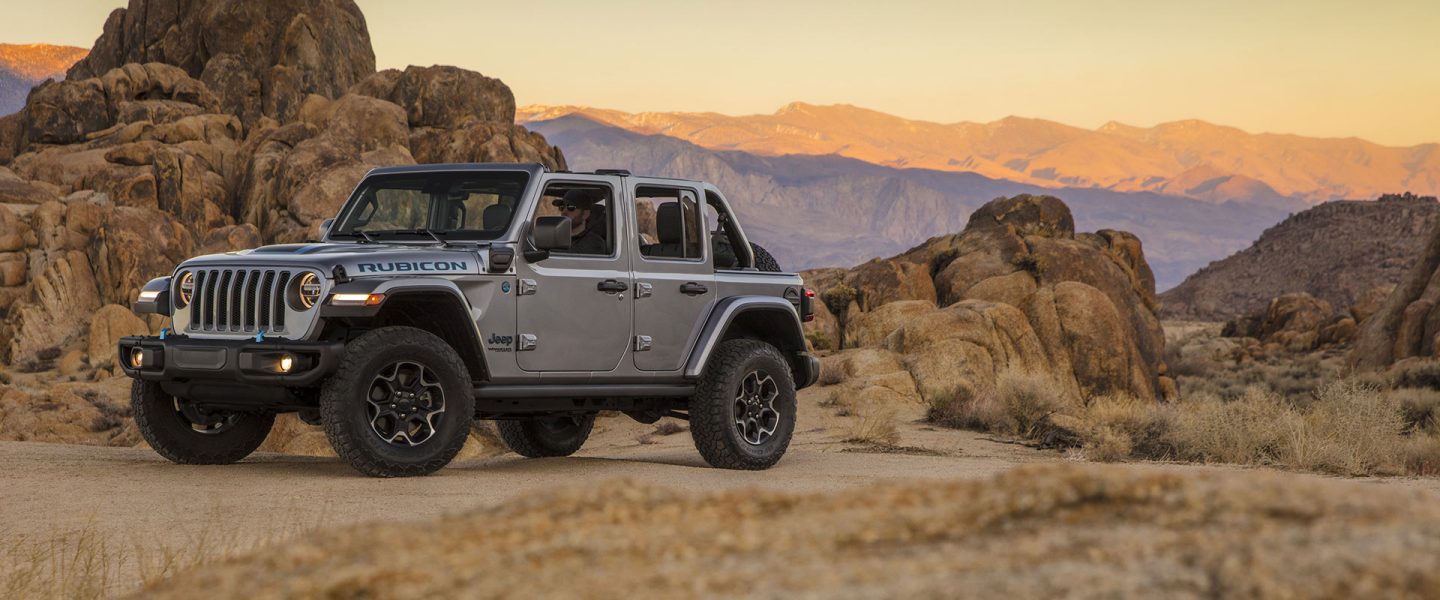 A gray 2021 Jeep Wrangler 4XE Rubicon parked on a trail in the mountains at sunset.