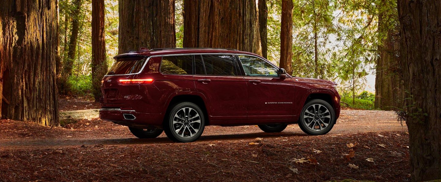 A three-quarter profile view of a 2021 Jeep Grand Cherokee L Overland parked off-road in the woods.