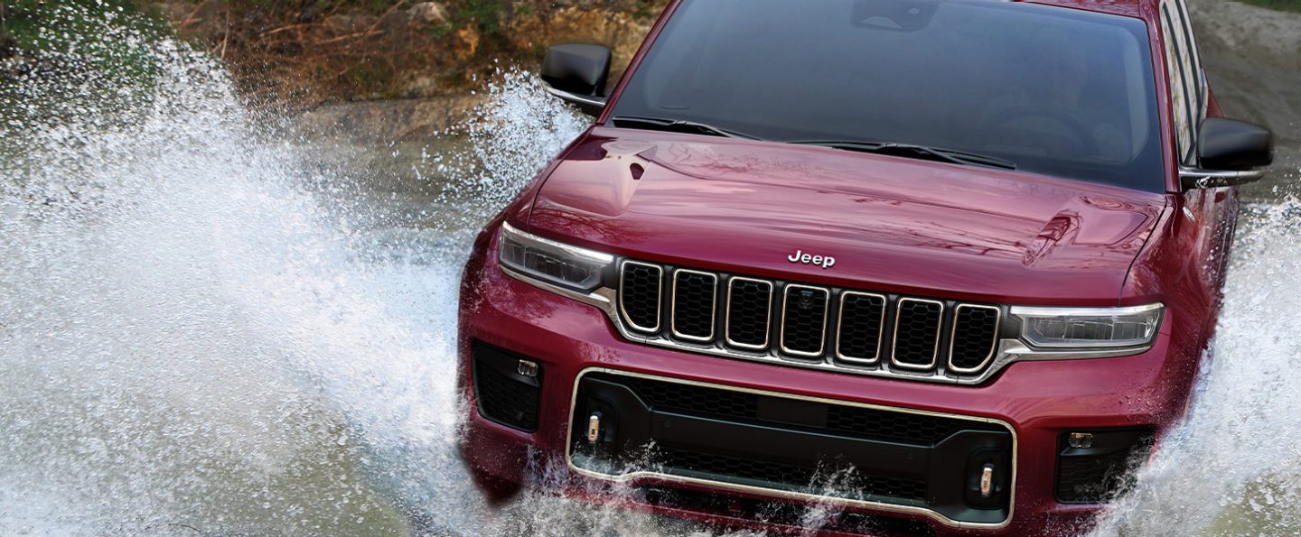 The 2021 Jeep Grand Cherokee L Overland being driven through water, throwing up waves that obscure its wheels entirely.