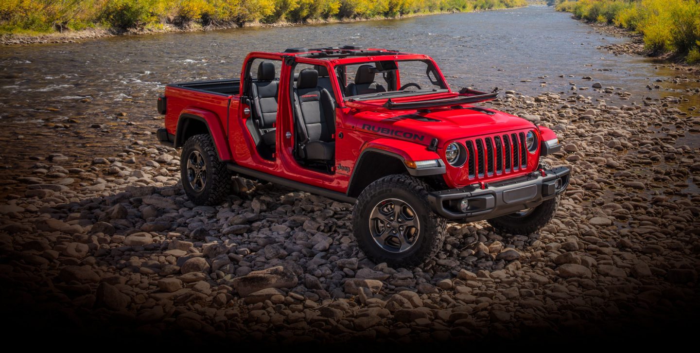 The 2022 Jeep Gladiator Rubicon with its doors off and windshield folded down, parked on a rocky beach.